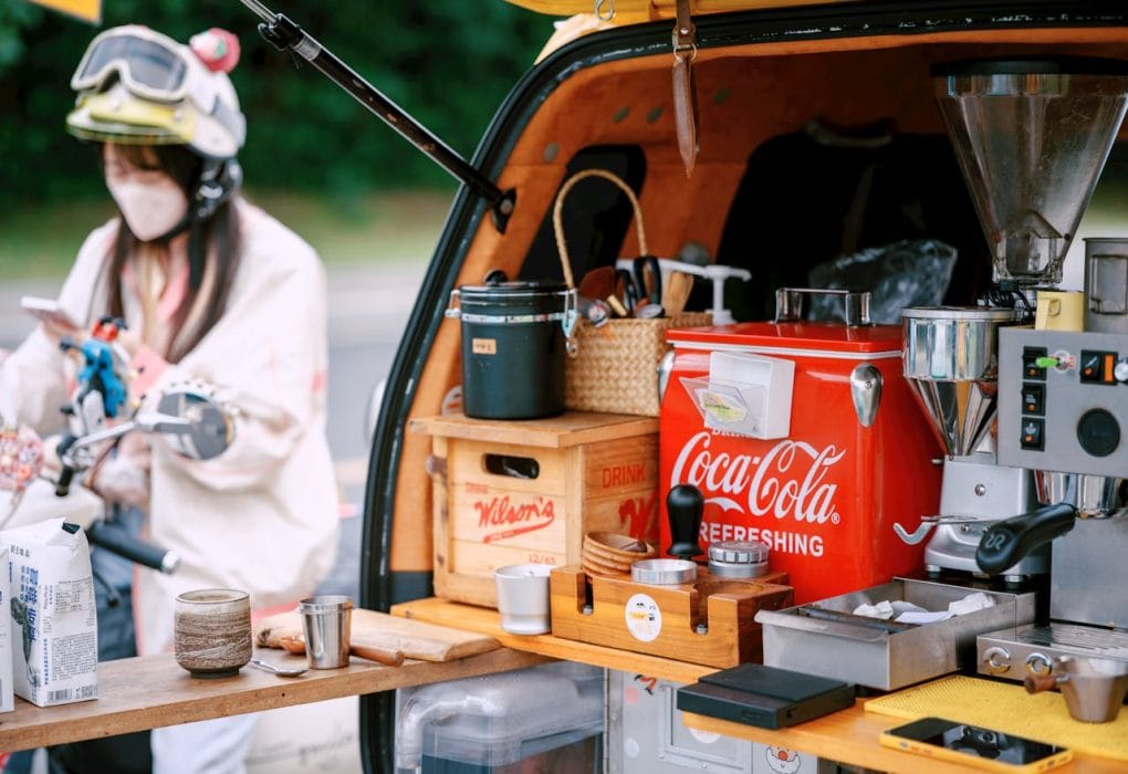 Mobile Kochstation auf Fahrradanhänger mit Kaffeemaschine, Getränkekühlschrank und Kochutensilien.